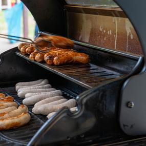 Grill mit verschiedenen Bratwürsten, einige sind braun gebraten, während andere noch roh sind.