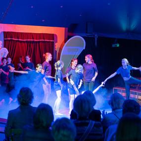 Acht Jugendliche führen eine Tanzaufführung in einem Zirkuszelt mit bunten Lichtern und Nebel auf.