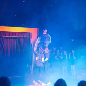 Akrobatinnen führen eine Pyramide auf der Bühne eines Zirkus, umgeben von Nebel und applaudierendem Publikum.