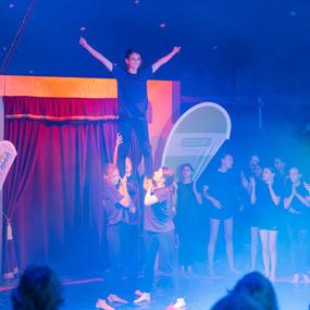 Akrobatik-Aufführung im Zirkus: Eine junge Frau steht auf den Händen von anderen Tänzerinnen in einem nebligen Umfeld.