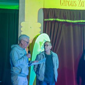 Zwei M&auml;nner stehen auf einer B&uuml;hne, einer spricht ins Mikrofon, der andere h&auml;lt ein Dokument in der Hand.