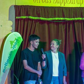 Zwei Personen stehen auf der B&uuml;hne im Circus ZappZarap und sprechen einander an, w&auml;hrend Zuschauer im Hintergrund beobachten.