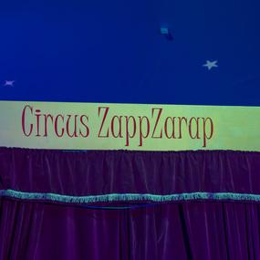 Bunte Bühne mit dem Schriftzug „Circus ZappZarap“ und einem purpurfarbenen Vorhang darunter.