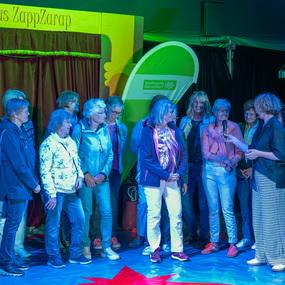 Gruppe von Frauen auf der B&uuml;hne des Circus ZappZarap, w&auml;hrend eine Frau mit Mikrofon spricht.