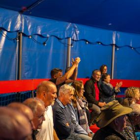 Menschen sitzen in einer Zirkushalle; einige applaudieren, andere schauen gespannt auf die B&uuml;hne.