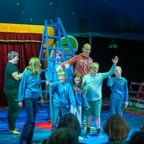 Sechs Kinder und ein Erwachsener stehen auf B&uuml;hne des Zirkus ZappZarap und winken l&auml;chelnd ins Publikum.