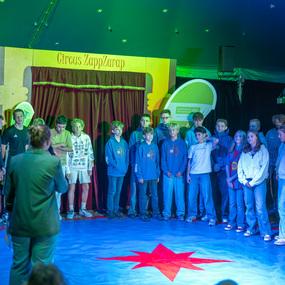 Gruppierung von Jugendlichen in blauen Sweatshirts auf einer Zirkusb&uuml;hne mit rotem Stern im Mittelpunkt.