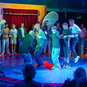 Gruppenspiel im Zirkuszelt mit mehreren Jugendlichen, die auf einer bunten Fl&auml;che um eine rote Markierung tanzen.