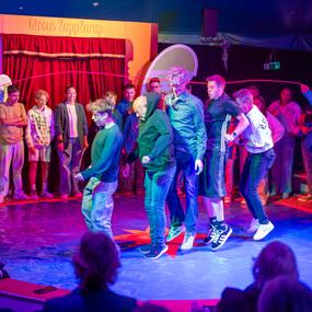 Menschen stehen auf einer bunten Zirkusmesse, w&auml;hrend sie miteinander an einem Spiel teilnehmen.