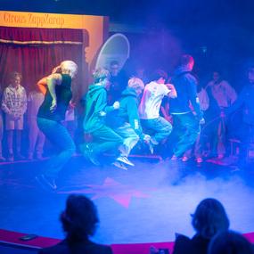 Gruppe von Kindern und Jugendlichen springt auf einer Zirkusb&uuml;hne, umgeben von Nebel und Publikum.