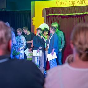 Gruppenszene im Zirkus mit mehreren Personen, die auf der B&uuml;hne stehen und miteinander sprechen, im Hintergrund ein roter Vorhang.