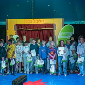 Gruppe von Jugendlichen auf einer B&uuml;hne im Zirkuszelt, die Urkunden und Geschenke halten.