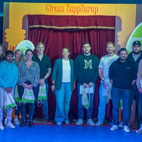 Gruppe von acht Personen steht vor einem roten Vorhang mit der Aufschrift &bdquo;Circus ZappZarap&ldquo; in einem Zirkuszelt.