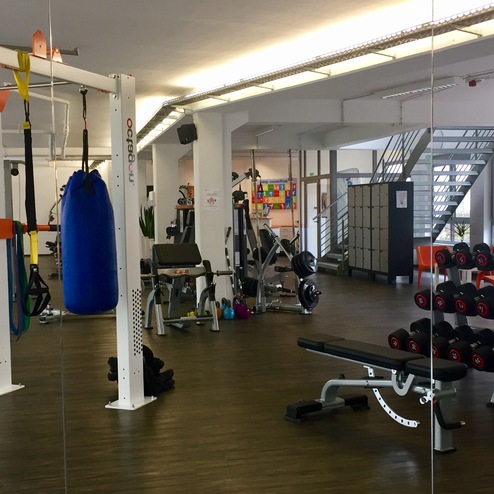 Fitnessstudio mit Gewichten, Halterungen, Fitnessgeräten und einem Boxsack in heller, moderner Umgebung.