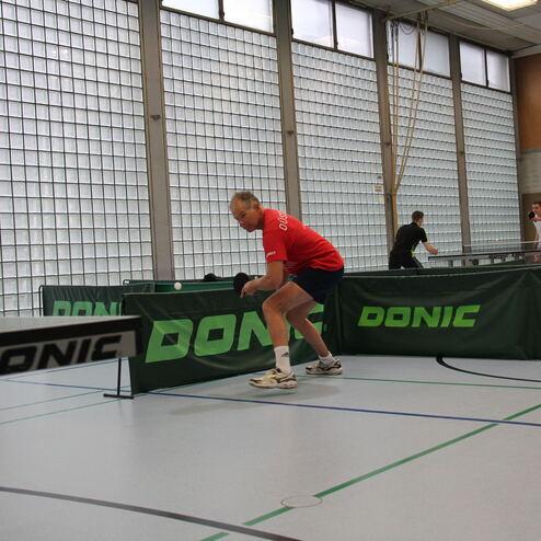 Ein Tischtennisspieler in rotem Shirt bereitet sich auf einen Schlag an einem Tischtennistisch vor.