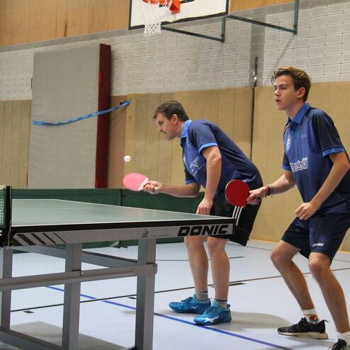 Zwei Tischtennisspieler stehen an einem Tisch und bereiten sich auf den Schlag eines Balls vor.