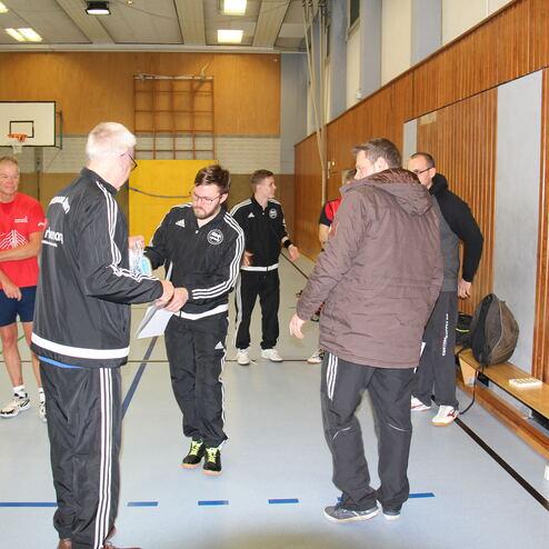 Gruppe von Sportlern in der Halle, einer übergibt einem anderen einen Preis, während weitere Teilnehmer zuschauen.