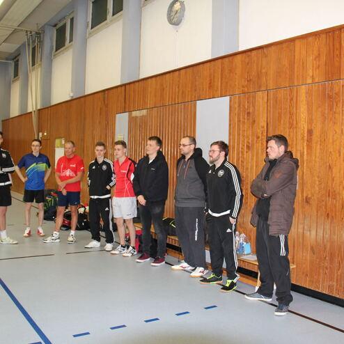Gruppe von sechs Sportlern in Sportkleidung steht an der Wand einer Halle, während ein Trainer spricht.