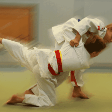 Zwei Kinder im Judoanzug führen einen Wurf im Training auf einer Tatami aus.