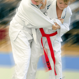 Zwei Kinder im Judogi kämpfen im Judowettbewerb auf einer Matte, eines trägt einen roten Gürtel.