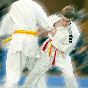 Zwei Jugendliche in Judokleidung kämpfen auf einer Matte, einer mit gelbem, der andere mit orangefarbenem Gürtel.