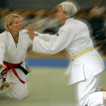 Zwei Judokas in Wettkampfkleidung üben eine Technik auf einer Judomatte. Beide Frauen sind im Mattenbereich aktiv.