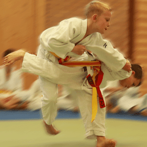 Zwei Kinder im Judoanzug führen einen Wurf im Judo auf einer matten Fläche aus.