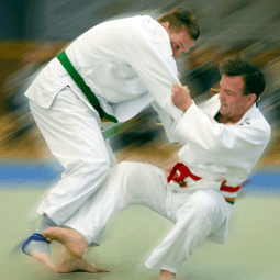 Zwei Judoka in weißen Anzügen kämpfen auf einer Matte, einer mit grünem und der andere mit rotem Gürtel.