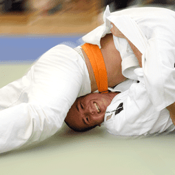Zwei Judokas ringen auf einer Matte, einer mit orangefarbenem Gurt, der andere mit blauem Gurt.