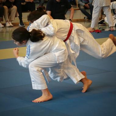 Zwei Judokas in wei&szlig;en Anz&uuml;gen &uuml;ben einen Wurf auf einer blauen Judomatte w&auml;hrend eines Wettkampfs.