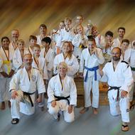 Gruppenfoto von Judoka in weißen Anzügen, einige halten Medaillen und Pokale, während andere lächeln.