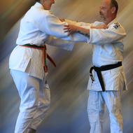 Zwei Judoka in weißen Anzügen üben Griffe im Training, der eine trägt einen schwarzen, die andere einen grünen Gürtel.