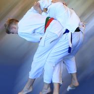 Zwei Judokas in weißen Anzügen führen einen Wurf in einem Sporttraining auf einer blauen Matte aus.