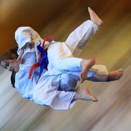 Zwei Judoka in weißen Uniformen führen einen Wurf aus, während sie auf einem verschwommenen Hintergrund in Bewegung sind.