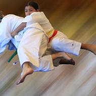 Zwei Judokas in weißem Gi führen einen Wurf aus, während sie in der Luft schwebend dargestellt sind.