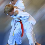 Zwei Kinder in Judoanzügen führen eine Judo-Technik aus, das hintere Kind greift den anderen von hinten an.