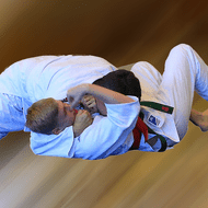 Zwei Jugendliche im Judoanzug kämpfen auf einer mattenbedeckten Fläche in dynamischer Bewegung.