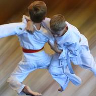 Zwei Kinder im Judoanzug kämpfen dynamisch in einem verschwommenen Umfeld.