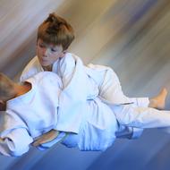 Zwei Kinder in weißen Judoanzügen führen einen Wurf im Spiel aus, während die Hintergrundfarbe sanft verschwommen ist.