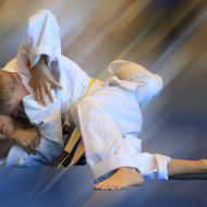 Zwei Kinder im Judogi kämpfen auf einer blauen Fläche, eines führt einen Haltegriff gegen das andere aus.