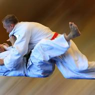 Zwei Personen im Judoanzug führen einen Wurf im Training aus, eine Person liegt auf dem Rücken.
