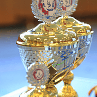 Zwei glänzende Pokale mit 2021er Auszeichnung auf einem Tisch, im Hintergrund unscharf.