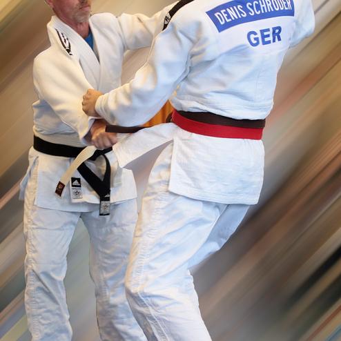 Zwei Judoka im Wettkampf, einer mit schwarzem und der andere mit rotem Gürtel, greifen sich an.
