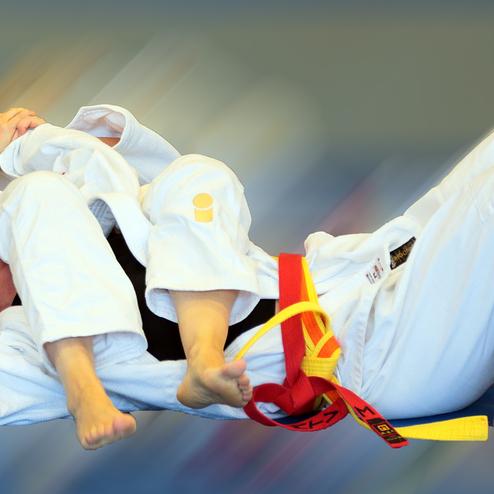 Zwei Judokas im Wettkampf, einer im Grappling, beide in weißen Judogis auf einer blauen Matte.