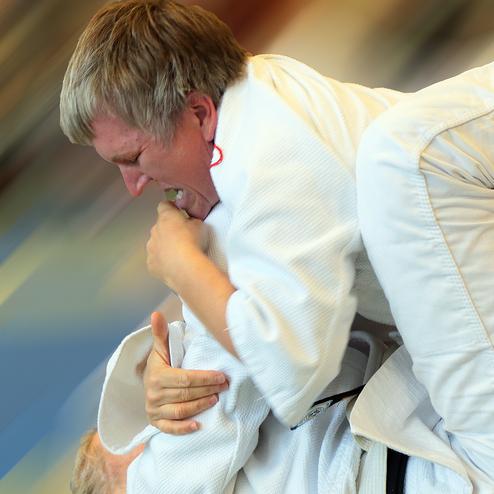 Zwei Judoka in weißen Anzügen kämpfen am Boden, einer greift den anderen an und hält ihn in einem Griff.