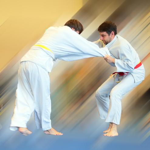 Zwei Judo-Kämpfer in weißen Anzügen kämpfen am Boden, einer trägt einen gelben, der andere einen roten Gürtel.