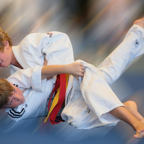 Zwei Kinder im Judoanzug führen einen Wurf im Training auf einer blauen Matte aus.