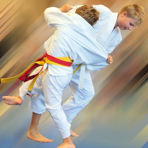 Zwei Kinder in weißen Judo-Anzügen führen eine Judo-Wurfbewegung auf einer blauen Matte aus.