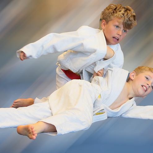 Zwei Jungen in weißen Judogi vollziehen einen Wurf, der eine dynamische Bewegung suggeriert.