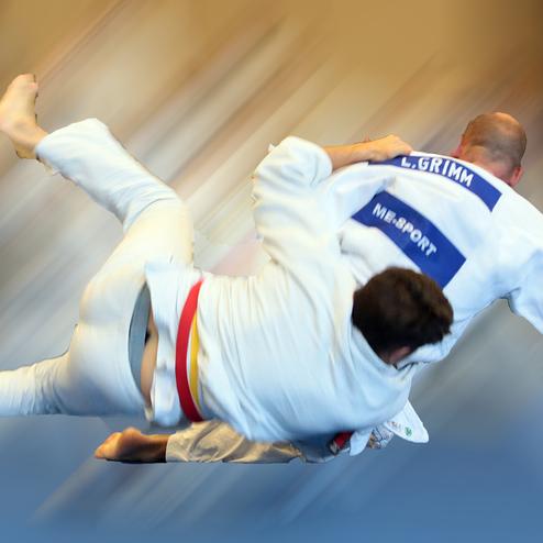 Zwei Judokas im Wettkampf; einer führt einen Wurf aus, während der andere auf dem Boden liegt.